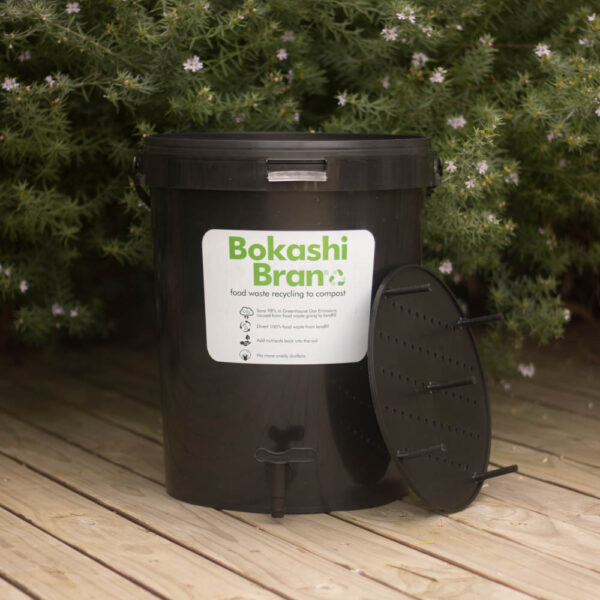The Bokashi Bran composting bucket displayed on a wooden deck with a plant in the background.